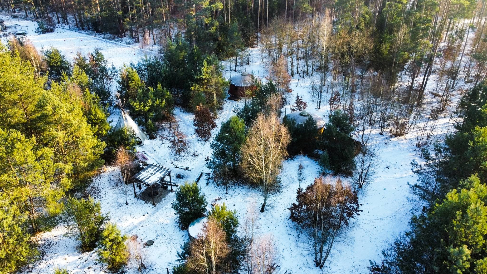 Zimowa panorama lasu z góry, jurty i palenisko na zaśnieżonej polanie